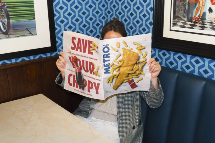 Person holding a newspaper with an image of fish and chips on the front cover