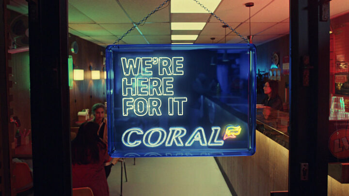 endframe for tv advert of neon sign on restaurant shop door that reads: We're here for it, Coral.