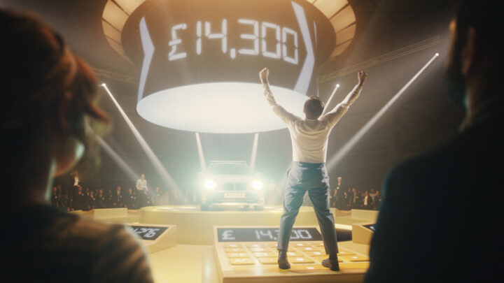 Car dealer celebrates winning whilst standing on a giant calculator with lots of shiny lights and fan fare happens around him