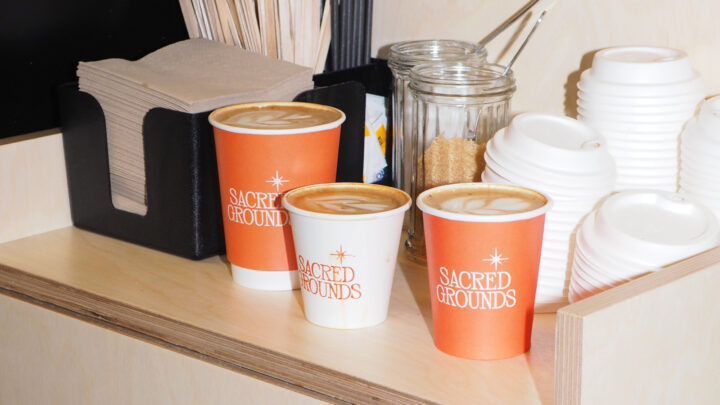 Sacred Grounds orange and white coffee cups on a counter with milk, sugar etc.