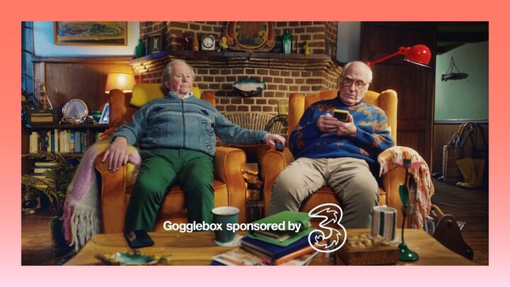 two men sit on reclining sofa chairs, one scrolling on their phone